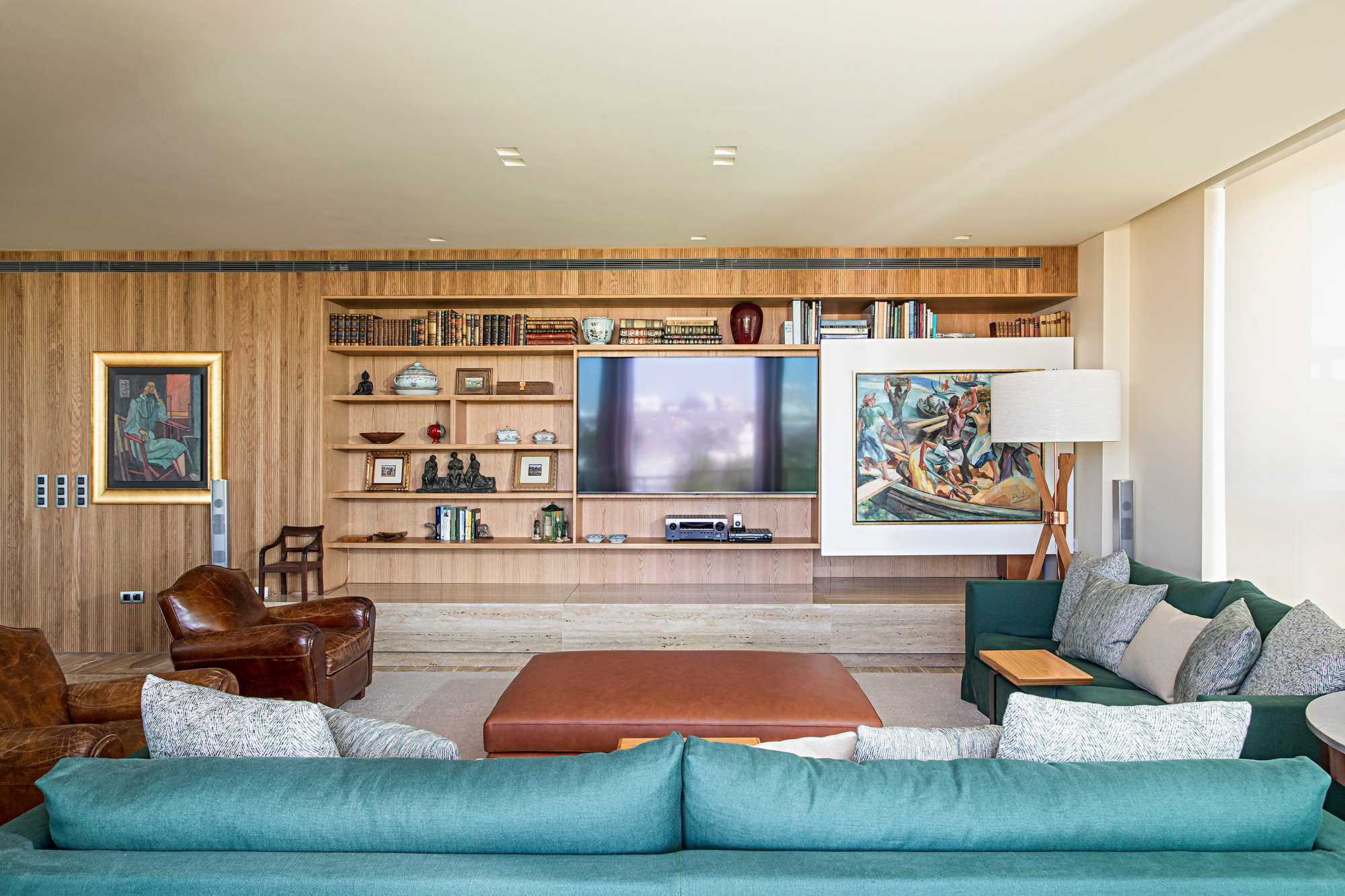 Painel deslizante esconde a TV na estante neste apartamento em Portugal. Projeto de Maurício Nóbrega. Na foto, sala de estar com tv escondida e sofás verdes.