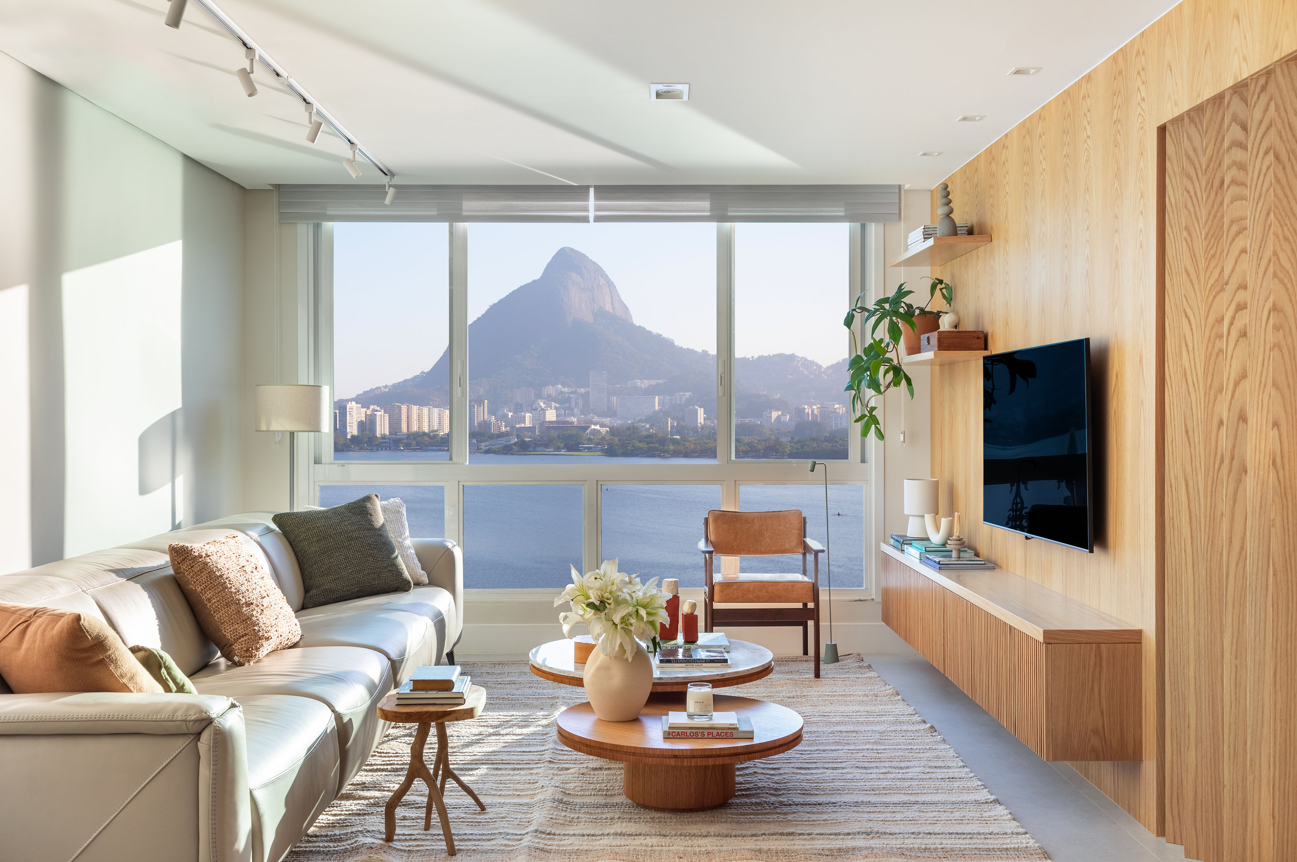 Apartamento de 190 m² tem vista para o Cristo Redentor de todos os cômodos. Projeto Beta Arquitetura. Na foto, sala de estar com tv, parede de madeira e vista para a lagoa.